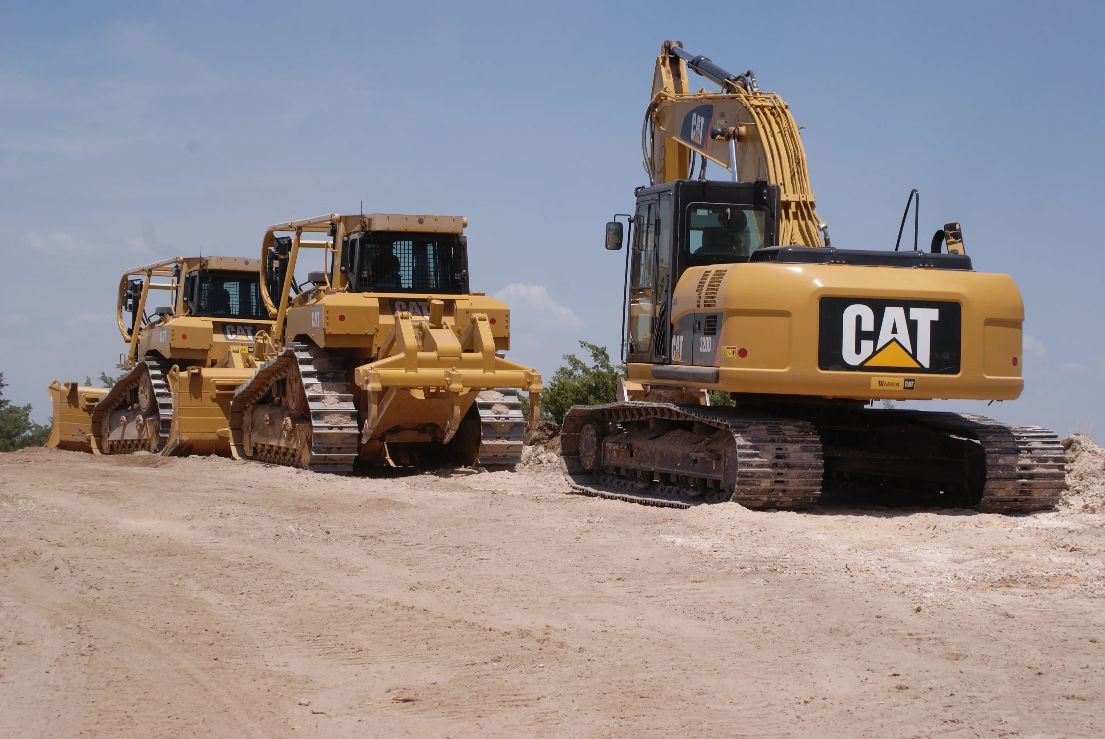 Two bulldozers and a CAT excavator parked on a sandy Florida job site