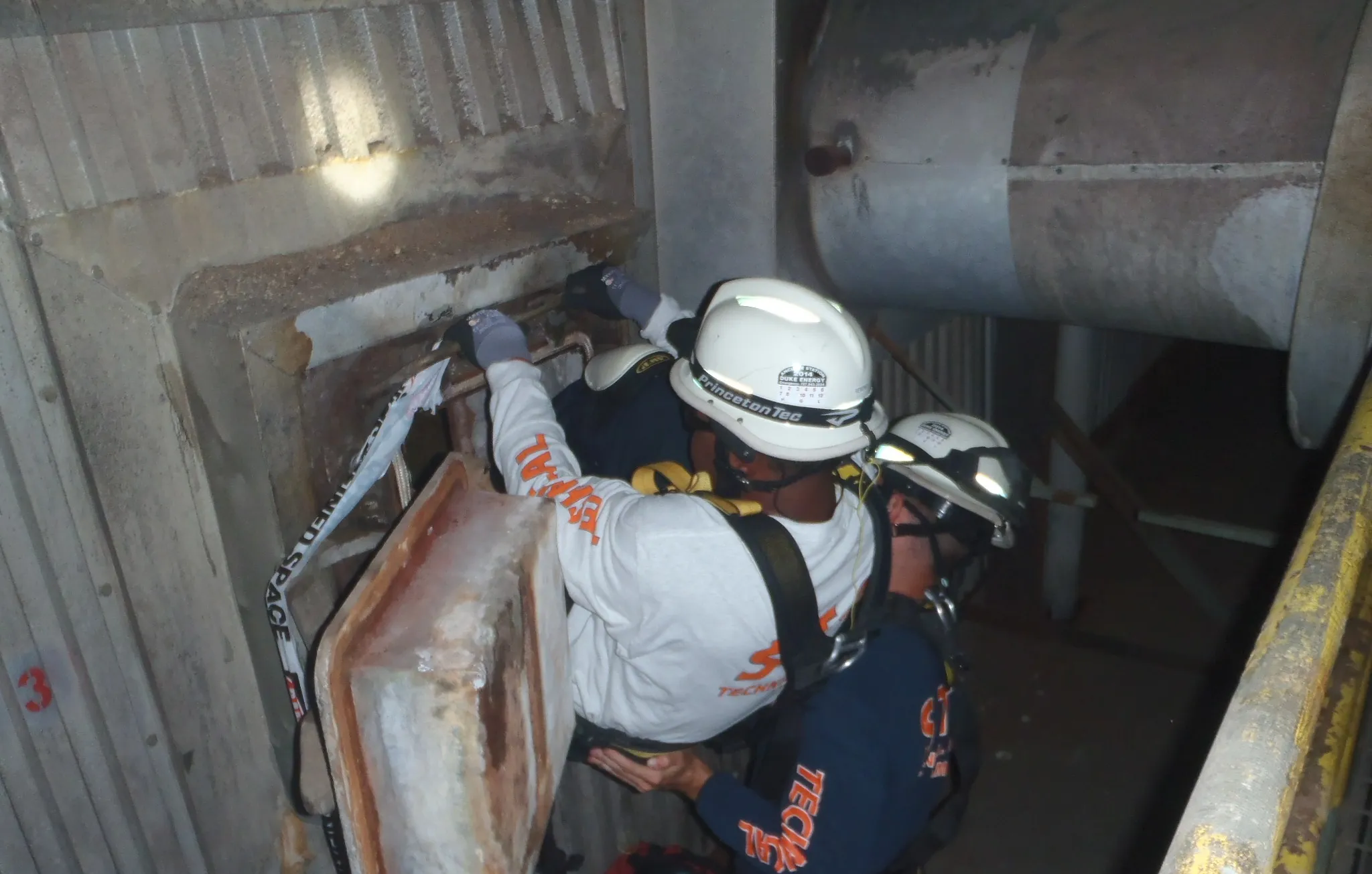 Rescuers in harnesses preparing to enter a confined space portal inside a plant