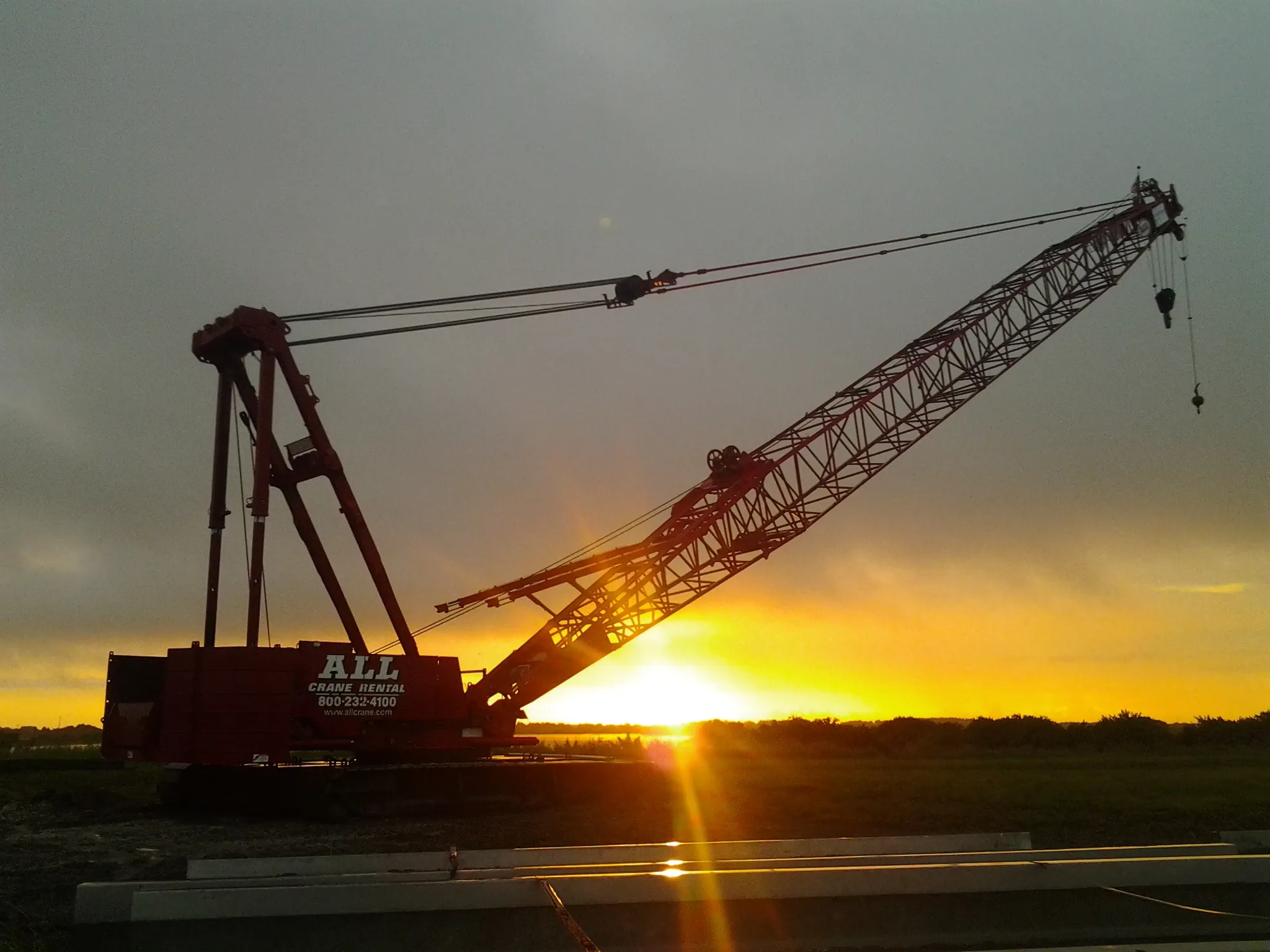 A lattice-boom crawler crane silhouetted against a Florida sunset