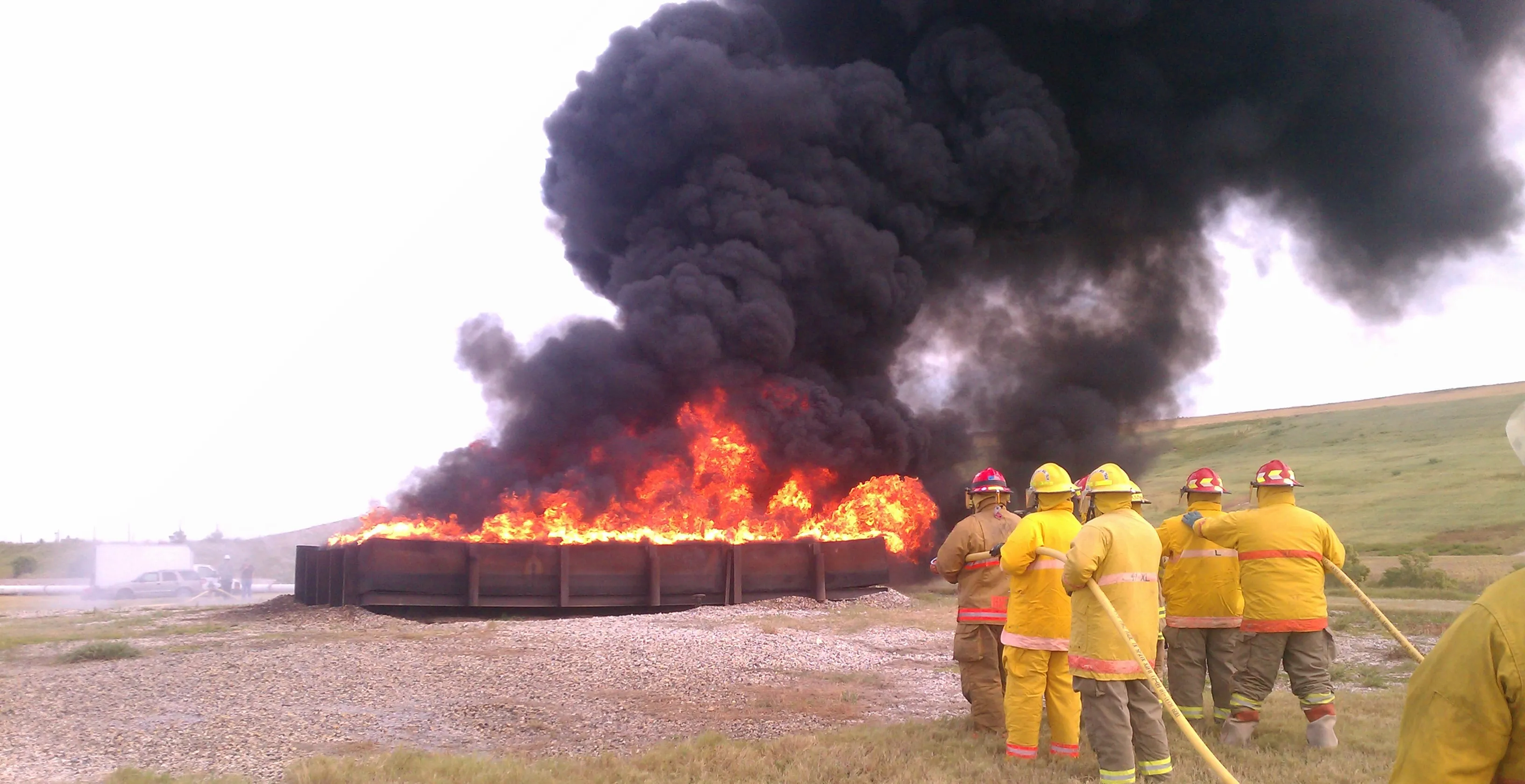 An industrial fire brigade hose team advancing on a live fire during STC training