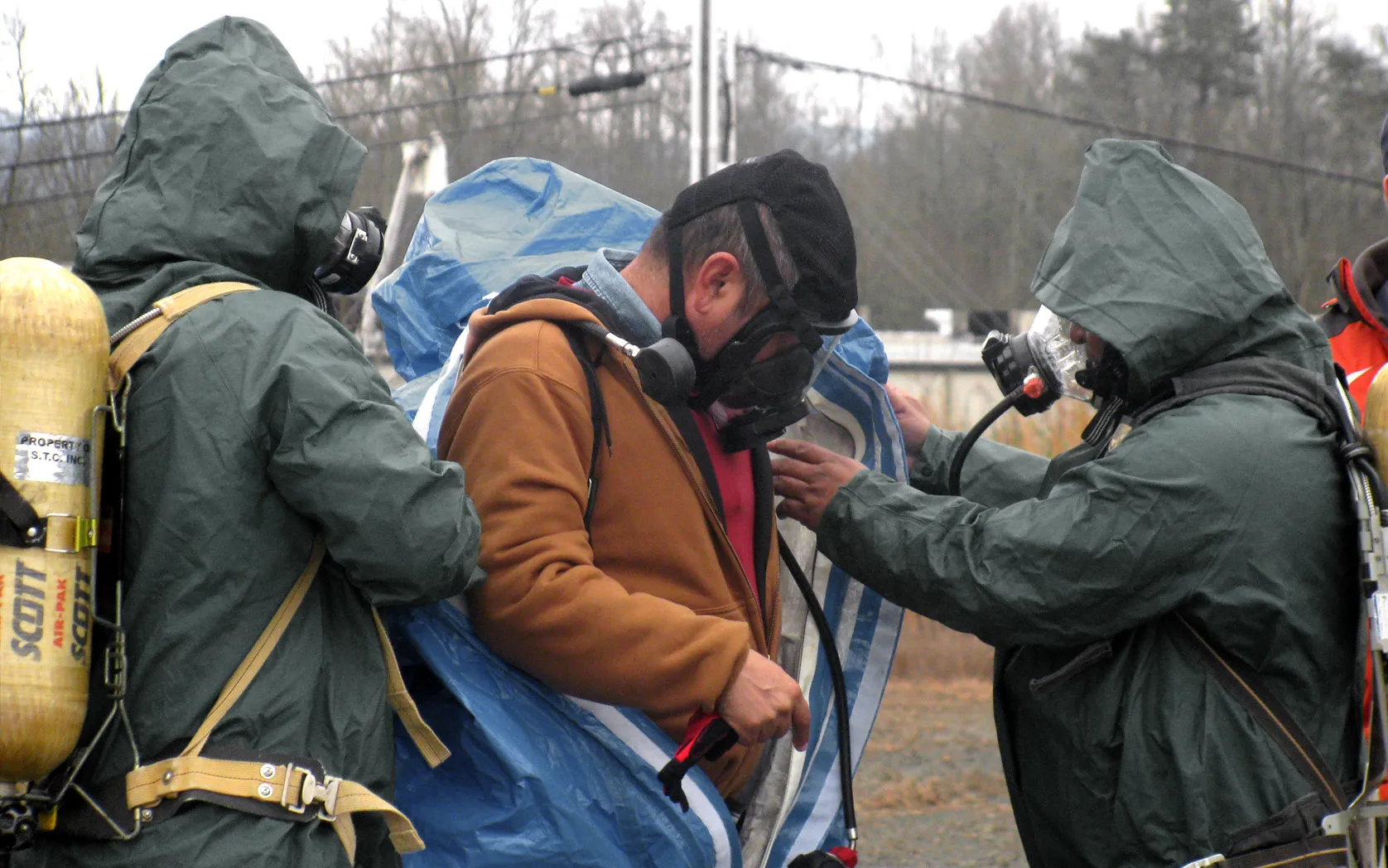 Responders on breathing air helping a teammate into a chemical protective suit